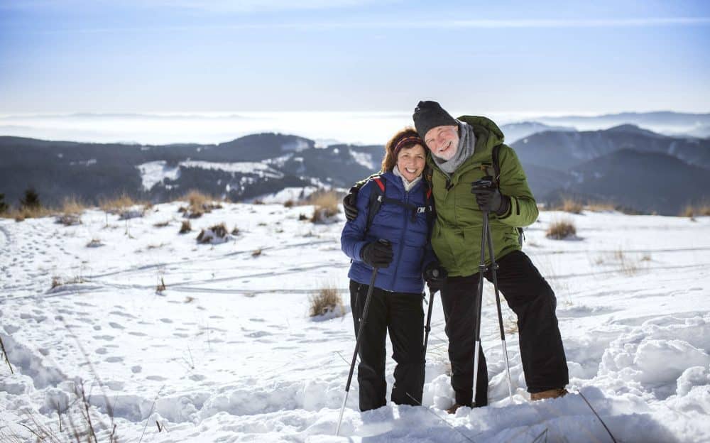 senior couple hikers with nordic walking poles in snow-covered winter nature.